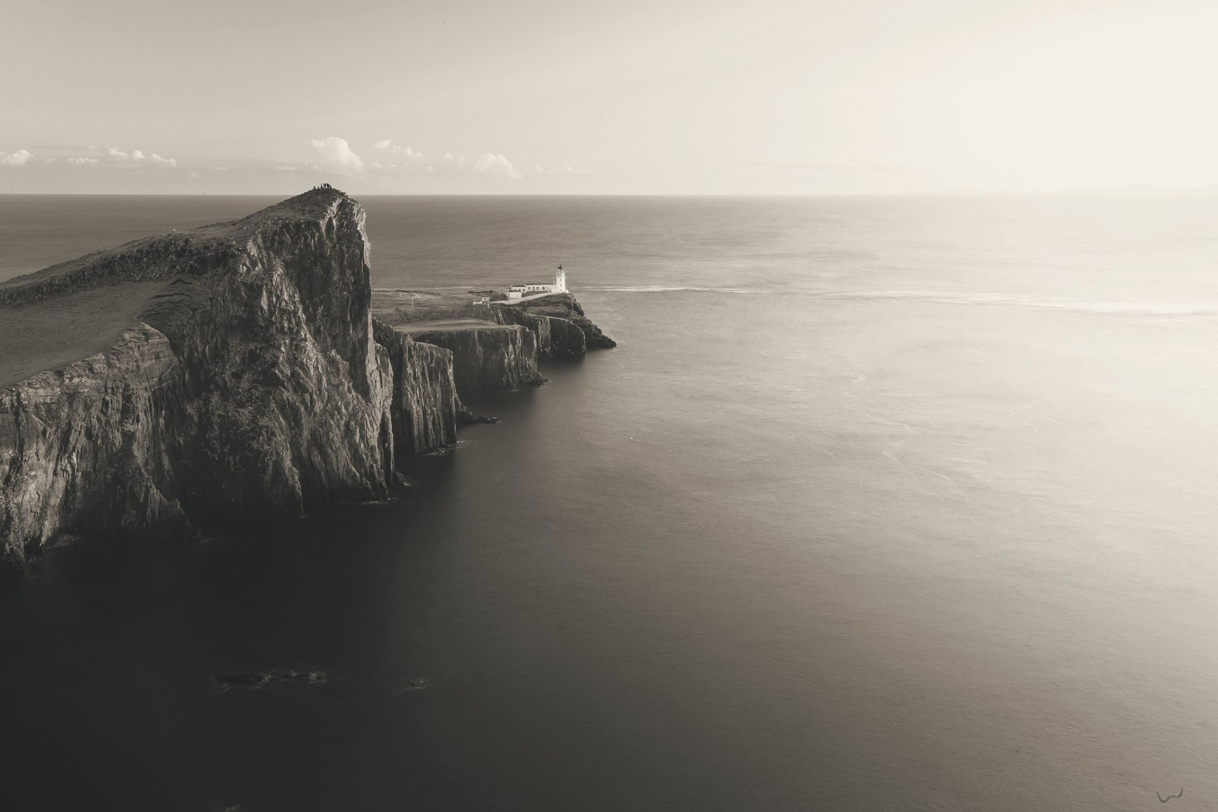 Zwart-witfoto van de kliffen en vuurtoren van Neist Point op Skye, boven een kalme zee
